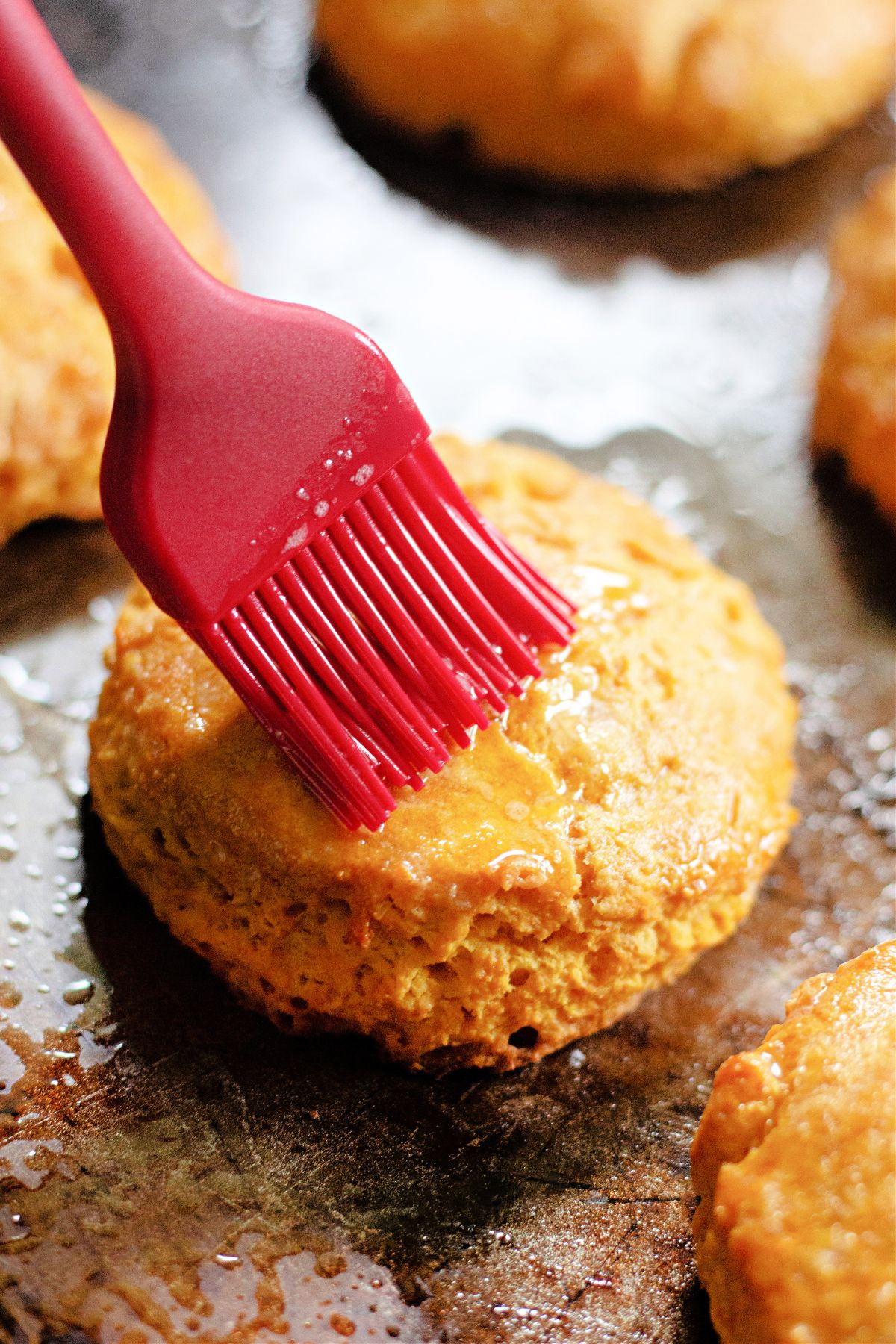 melted butter being brushed on top of biscuits on a baking sheet.