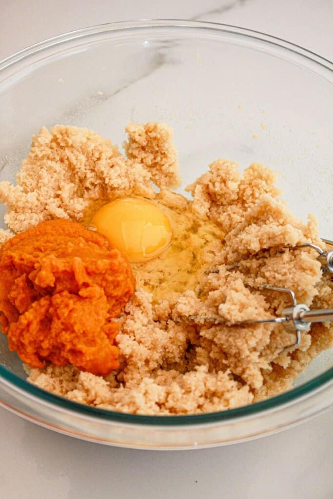 egg and pumpkin being mixed into dough in a glass mixing bowl.