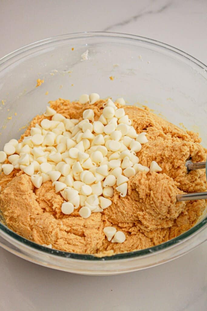 white chocolate chips being folded into dough in a glass mixing bowl.