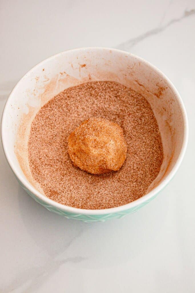 cookie dough ball being rolled in cinnamon sugar.