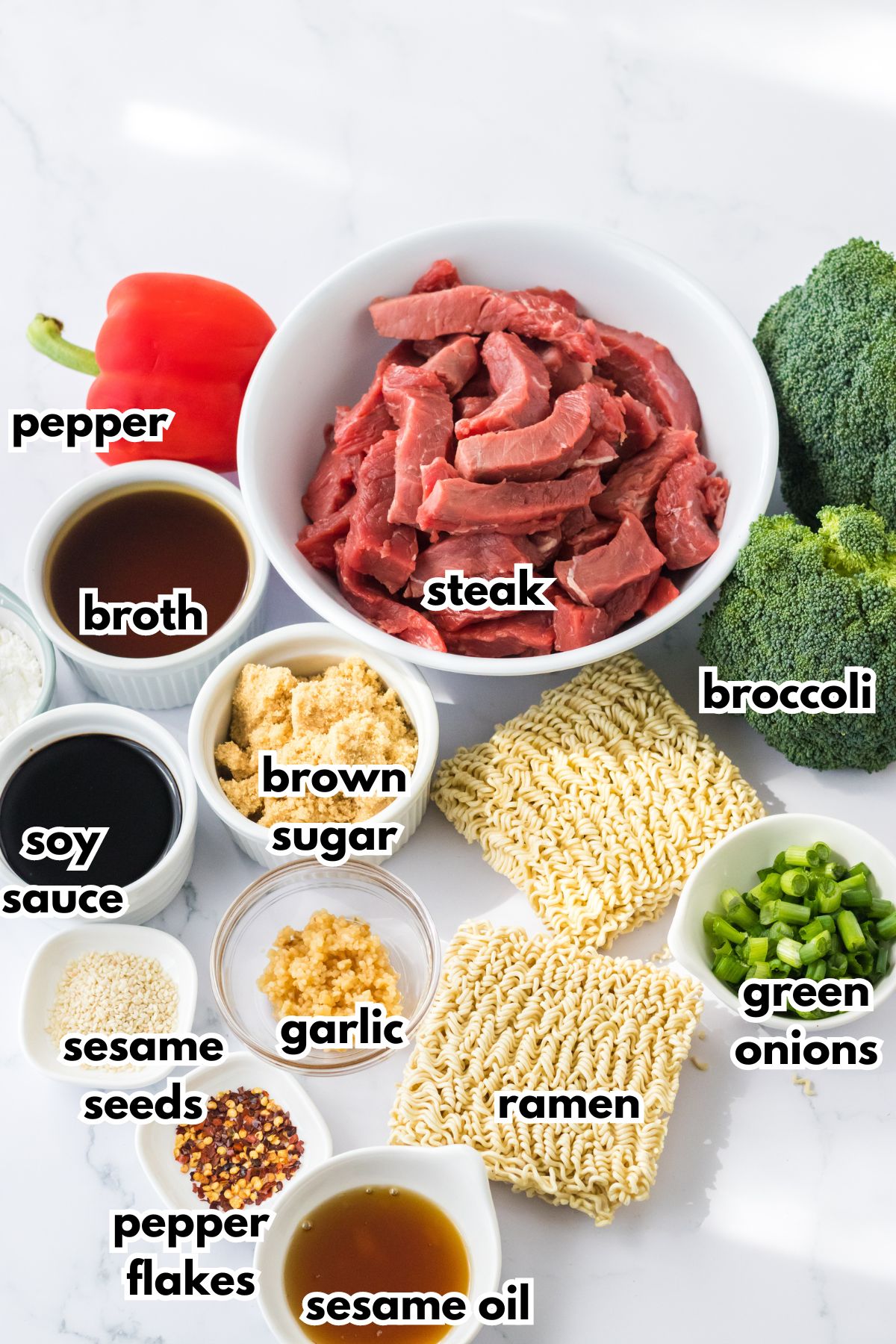 bowls of steak, pepper, broth, soy sauce, brown sugar, sesame seeds, garlic, pepper flakes, sesame oil, ramen, green onions, and broccoli on a counter.