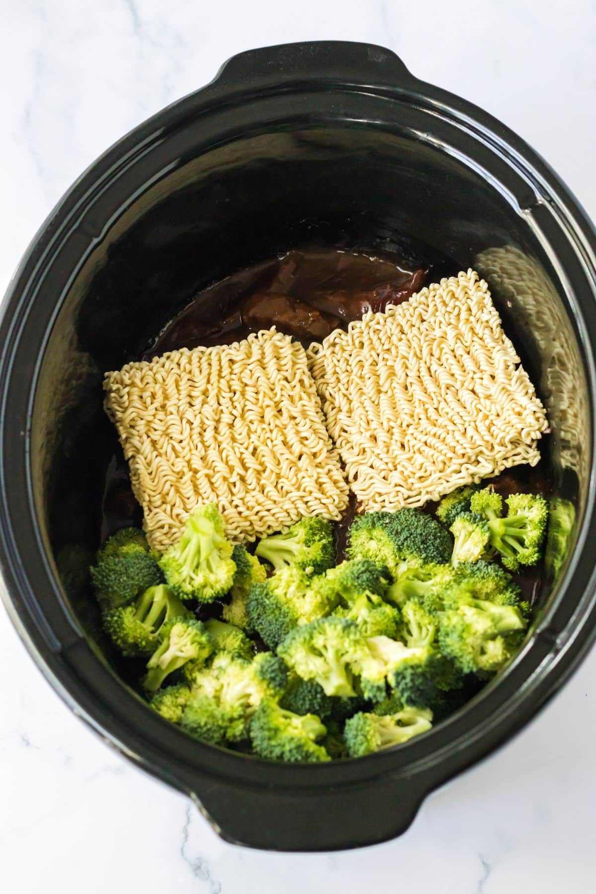 Noodles and broccoli being added to the crockpot.