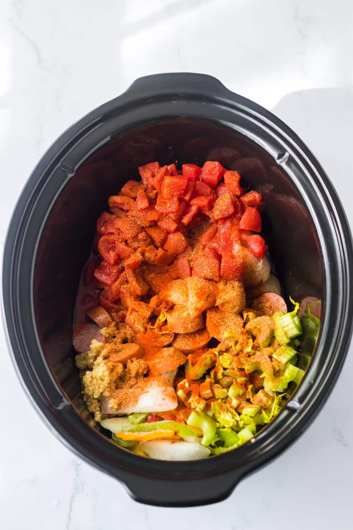 Tomatoes, frozen veggies, chicken, sausage, and seasonings added to the crockpot.