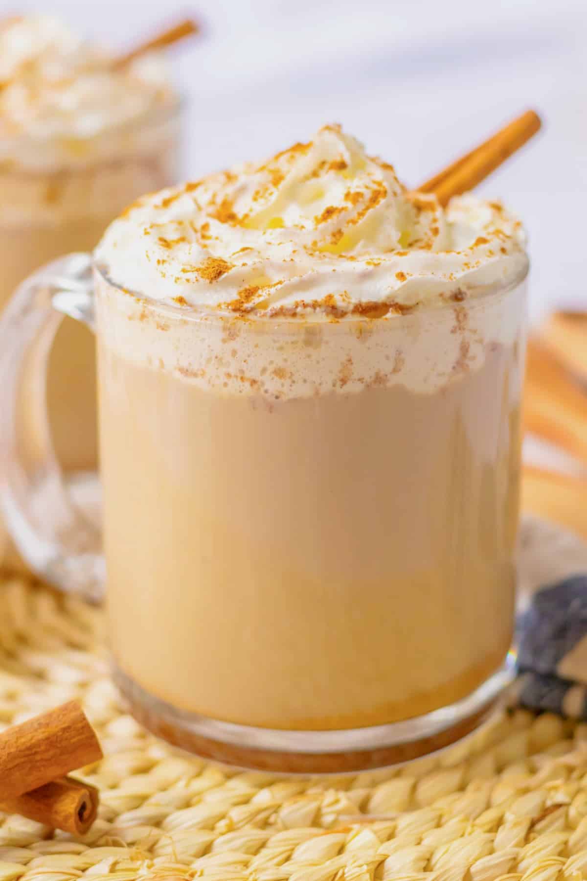 Slow cooker pumpkin spice latte in a glass mug topped with a cinnamon stick.