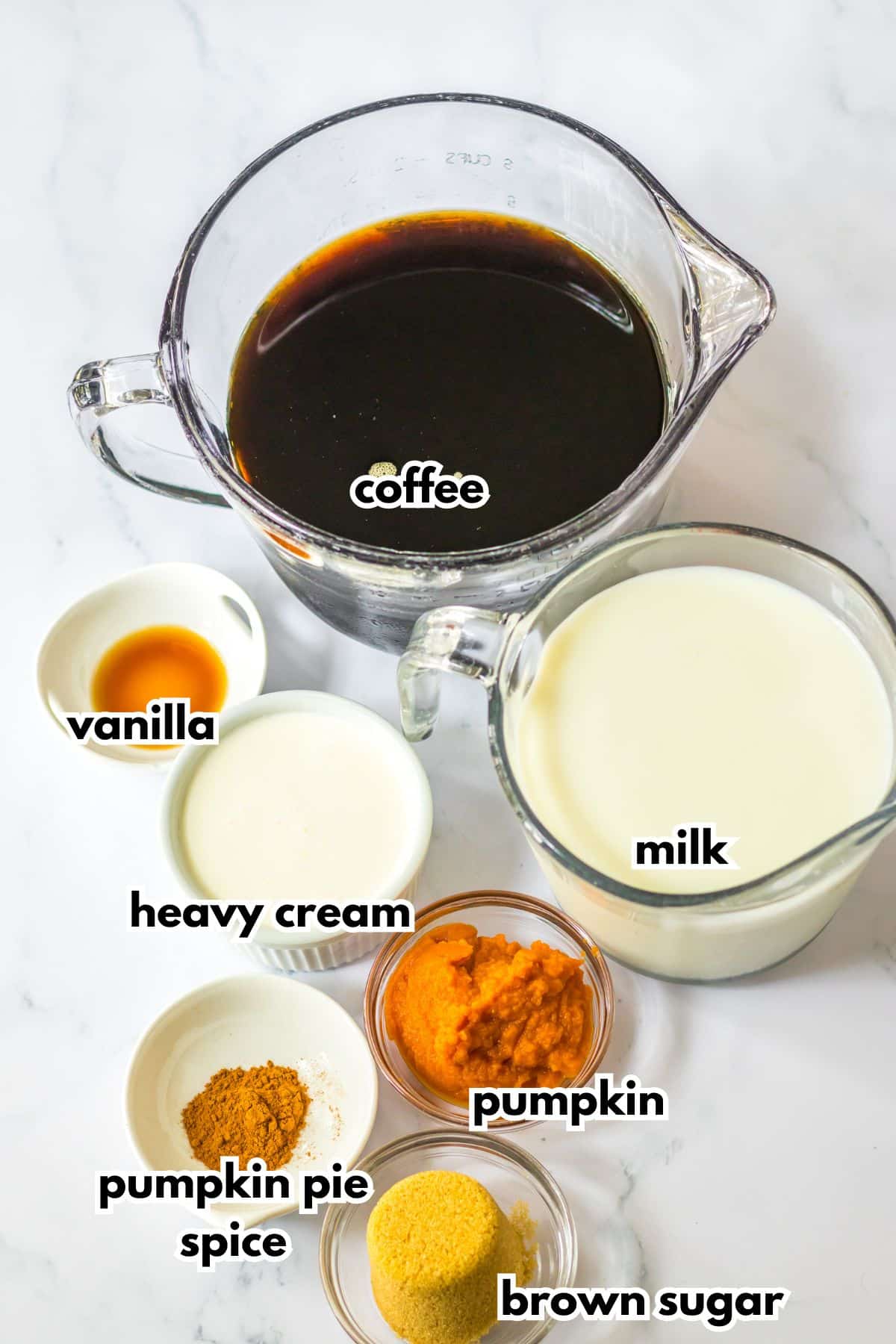 Bowls of coffee, vanilla, heavy cream, pumpkin pie spice, brown sugar, pumpkin, and milk on a counter.