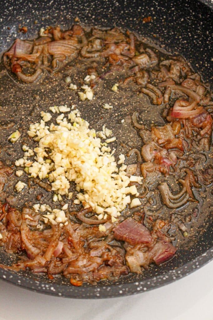 garlic being added to cooked shallots in a large skillet.