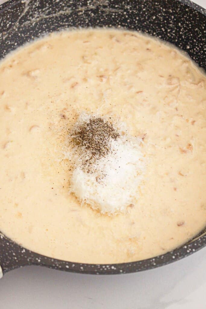 seasonings being added to cream sauce in a large skillet.