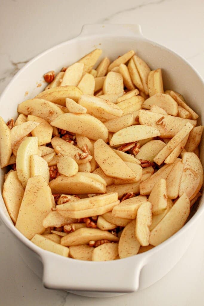 Apple slices and pecans in a casserole dish on a counter.