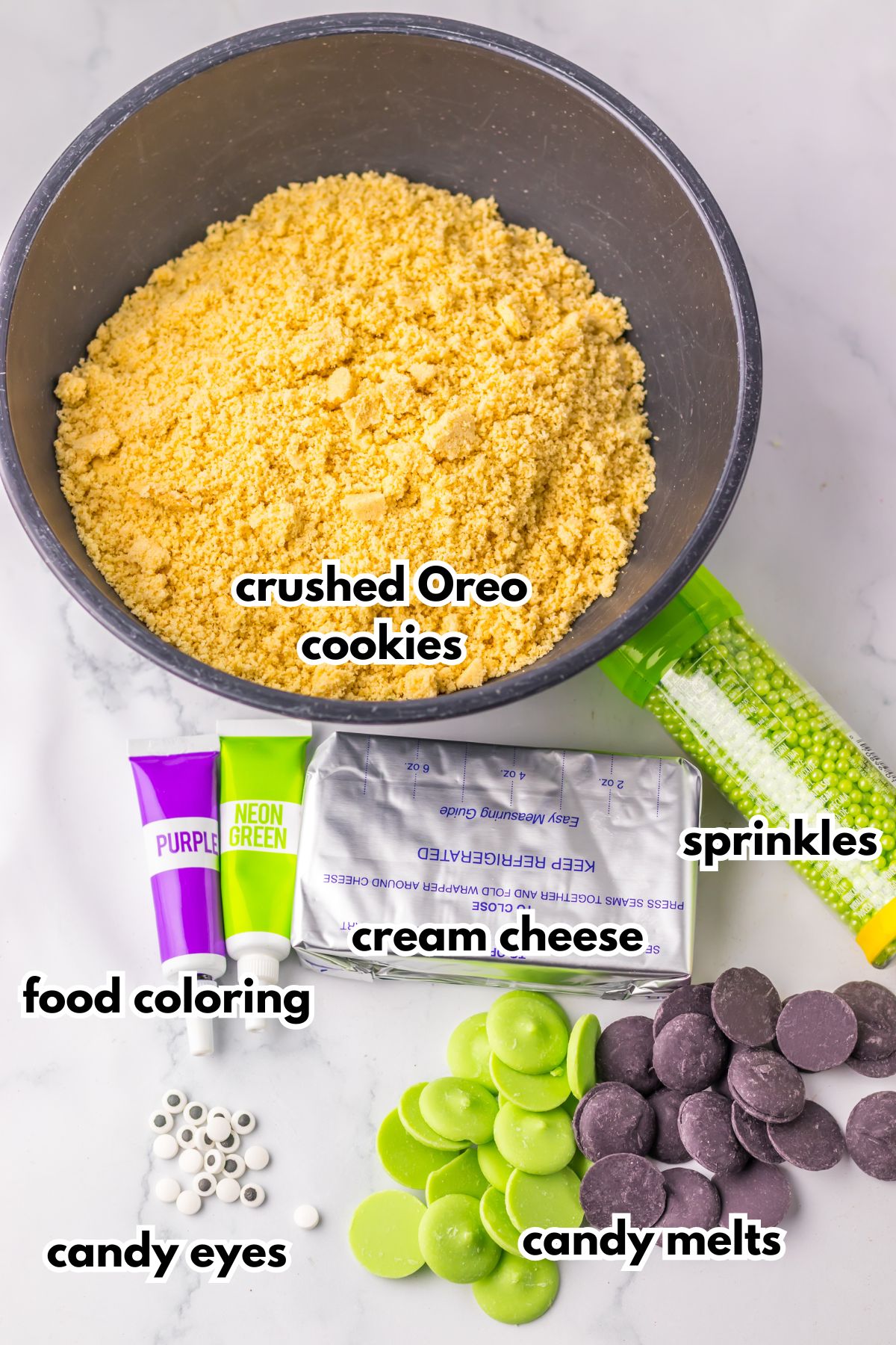 Bowls of crushed oreo cookies, food coloring, cream cheese, sprinkles, candy eyes, and candy melts on a counter.
