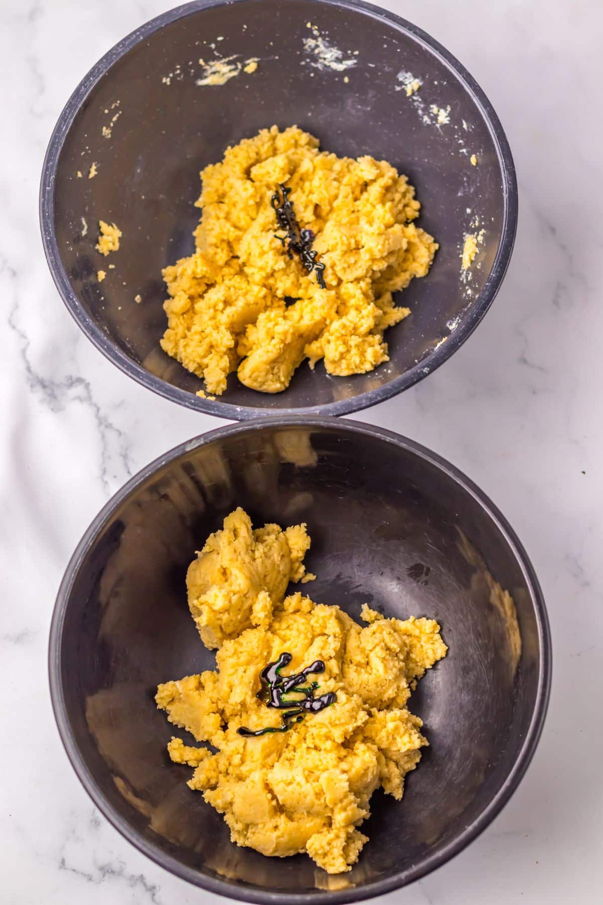 Cookie and cream cheese mixture in two seperate bowls being dyed green and purple.