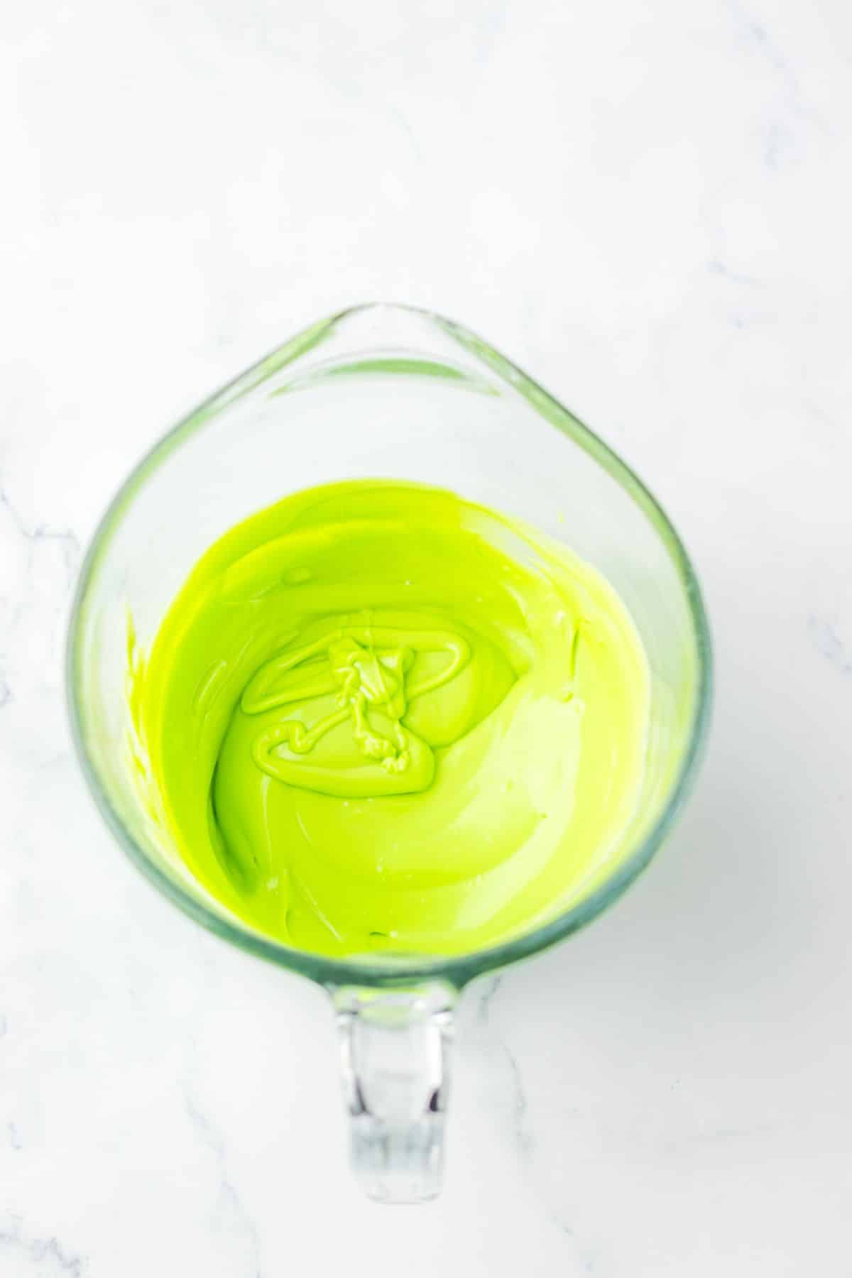 Green candy melts being melted in a glass measuring cup.