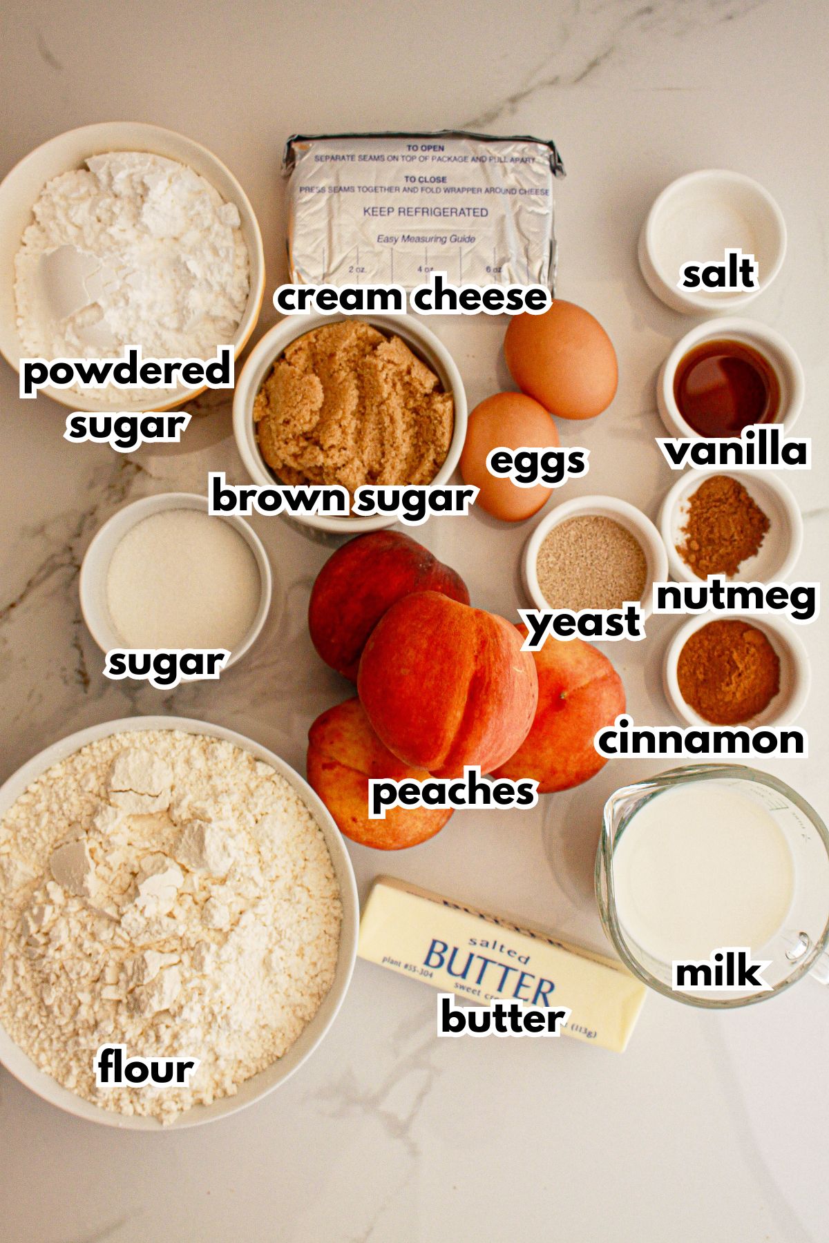 Bowls of powdered sugar, cream cheese, salt, eggs, vanilla, yeast, nutmeg, cinnamon, milk, butter, peaches, flour, and sugar on a counter.