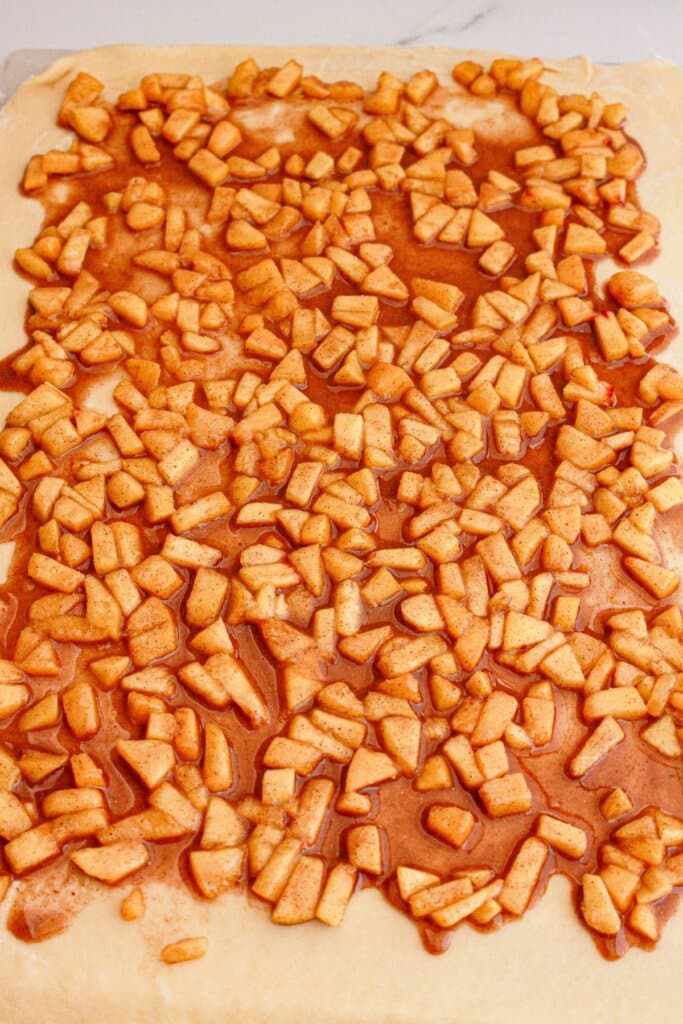 Peaches being spread on top of rolled out dough.