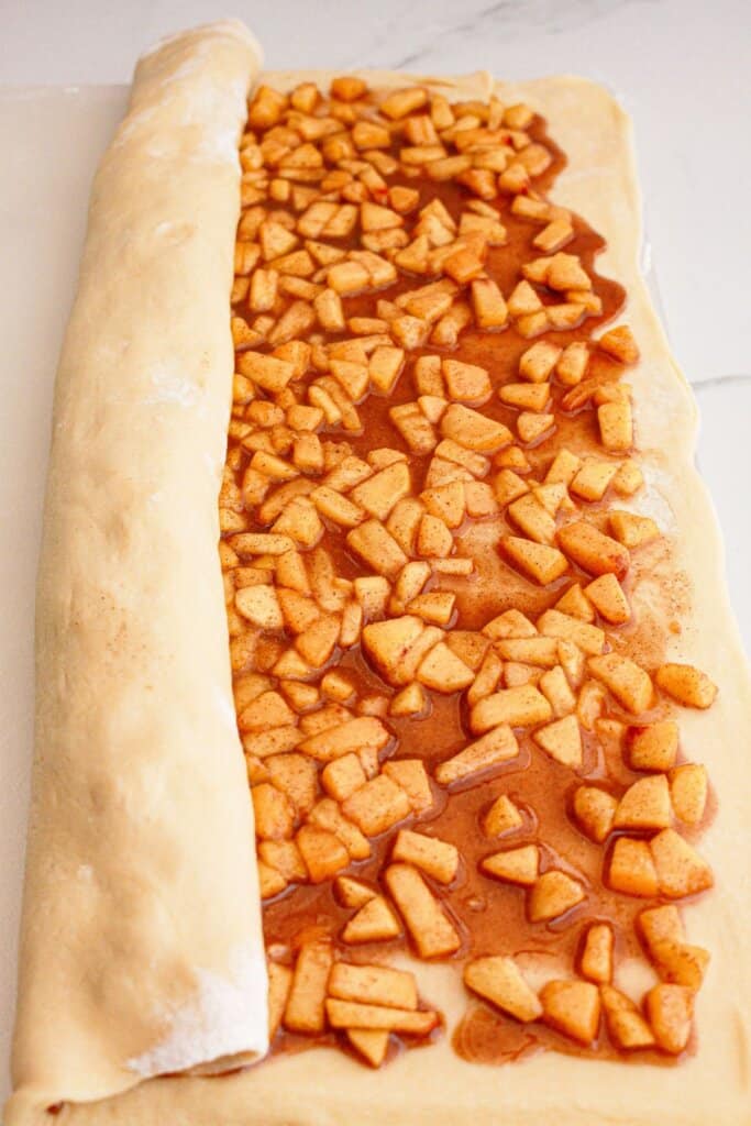 Peaches spread on top of the dough, and being rolled tightly.