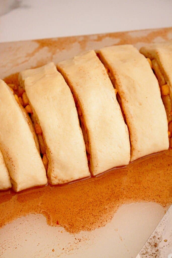 Cinnamon roll dough being cut into slices on a wooden cutting board.