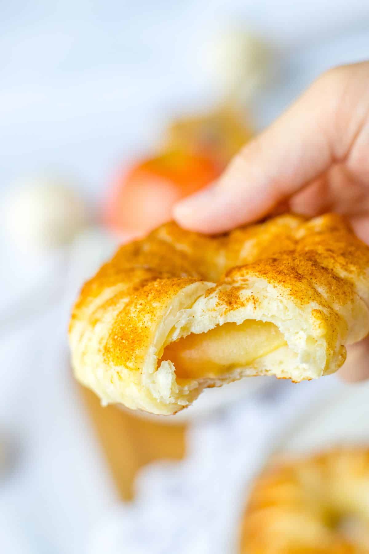 Puff pastry apple doughnut with a bite misisng held in the air.