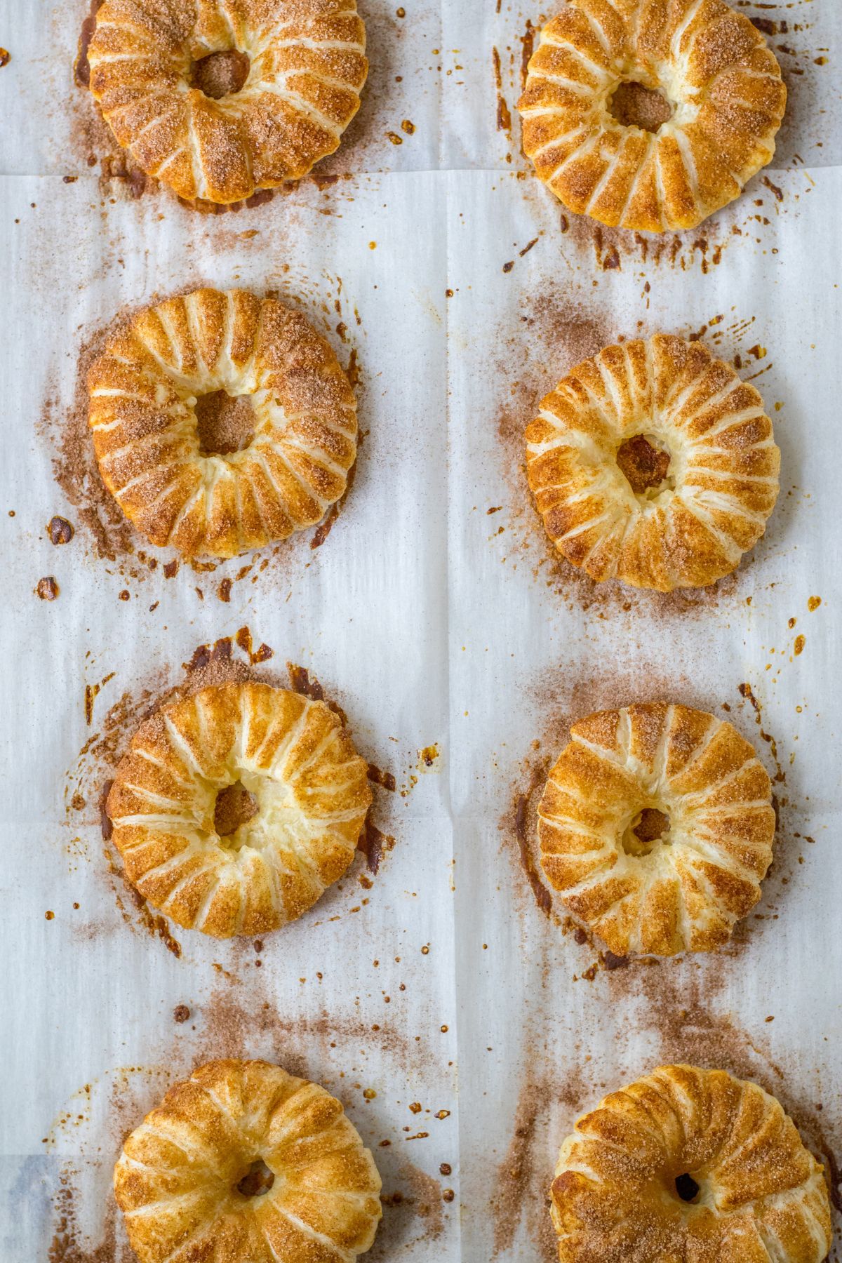 Baked puff pastry apple doughnuts on a parchment lined baking sheet.