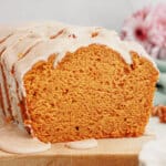 Pumpkin Bread With Cinnamon Glaze Loaf of pumpkin bread being drizzled with cinnamon glaze on a wooden cutting board with a slice missing.