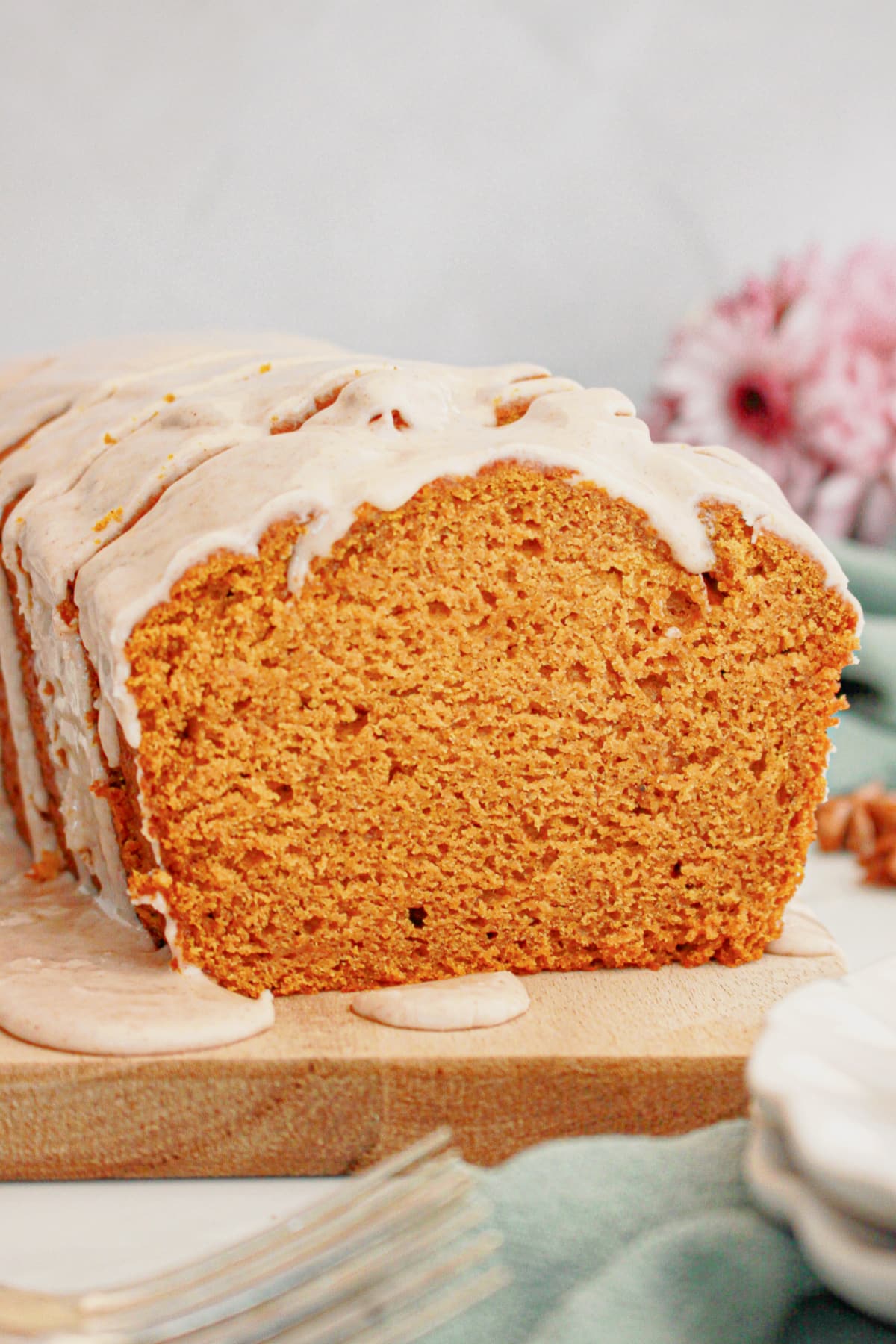 Loaf of pumpkin bread being drizzled with cinnamon glaze on a wooden cutting board with a slice missing.