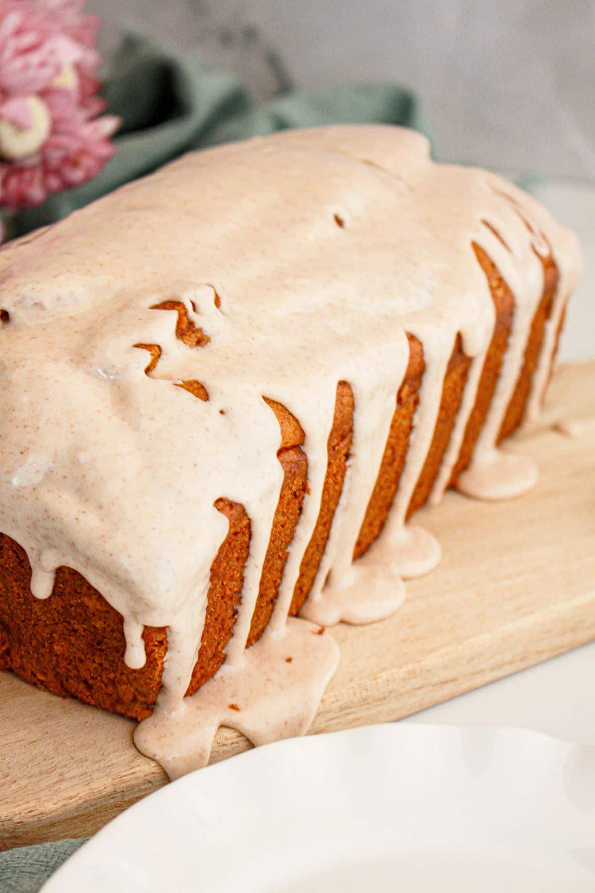 Loaf of pumpkin bread being drizzled with cinnamon glaze on a wooden cutting board.