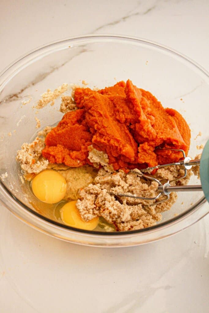 Wet ingredients being mixed in a glass mixing bowl with a hand mixer.