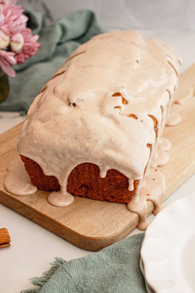 Loaf of pumpkin bread being drizzled with cinnamon glaze on a wooden cutting board.