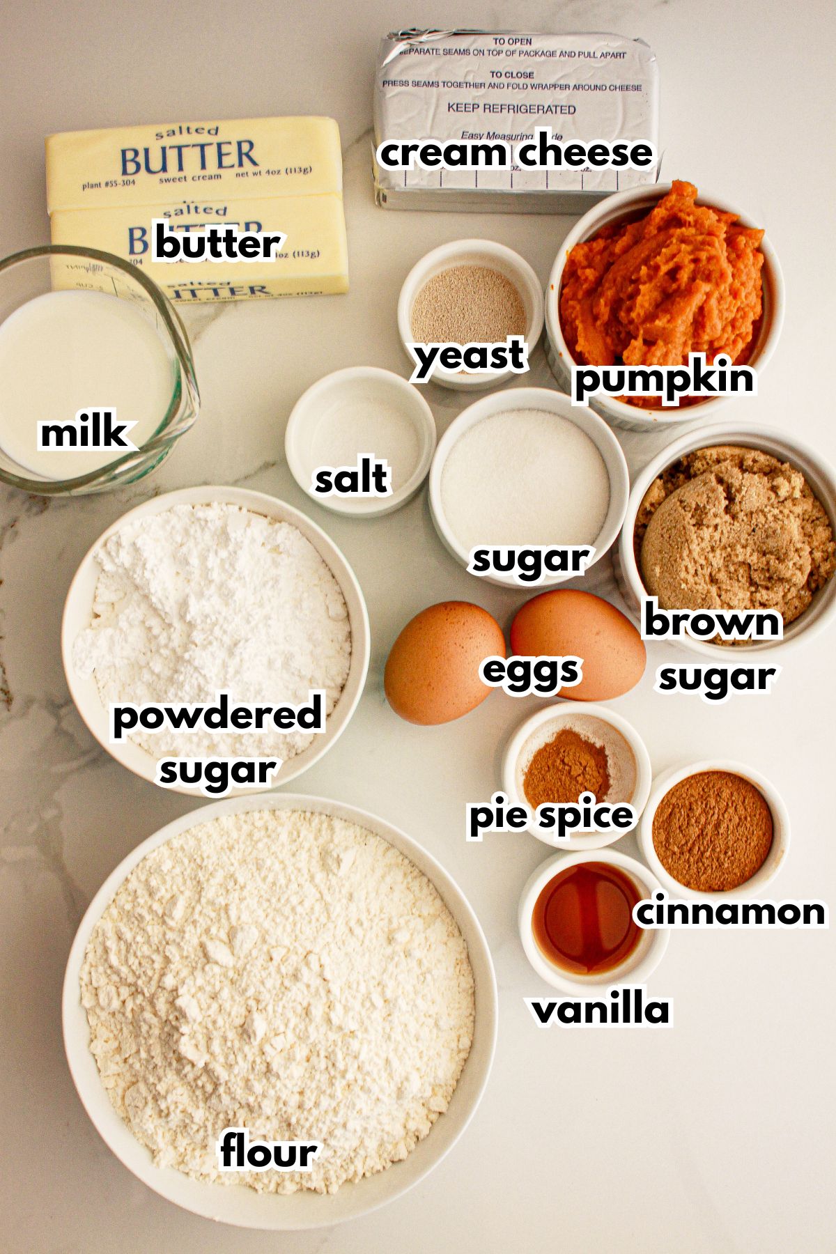 Bowls of butter, cream cheese, milk, yeast, pumpkin, salt, sugar, powdered sugar, eggs, pie spice, cinnamon, vanillla, and flour.