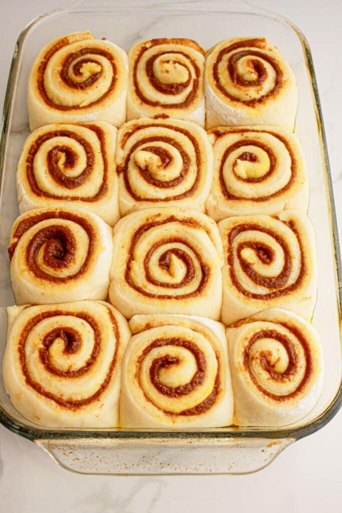 Baked unfrosted cinnamon rolls in a glass baking dish ready to bake.