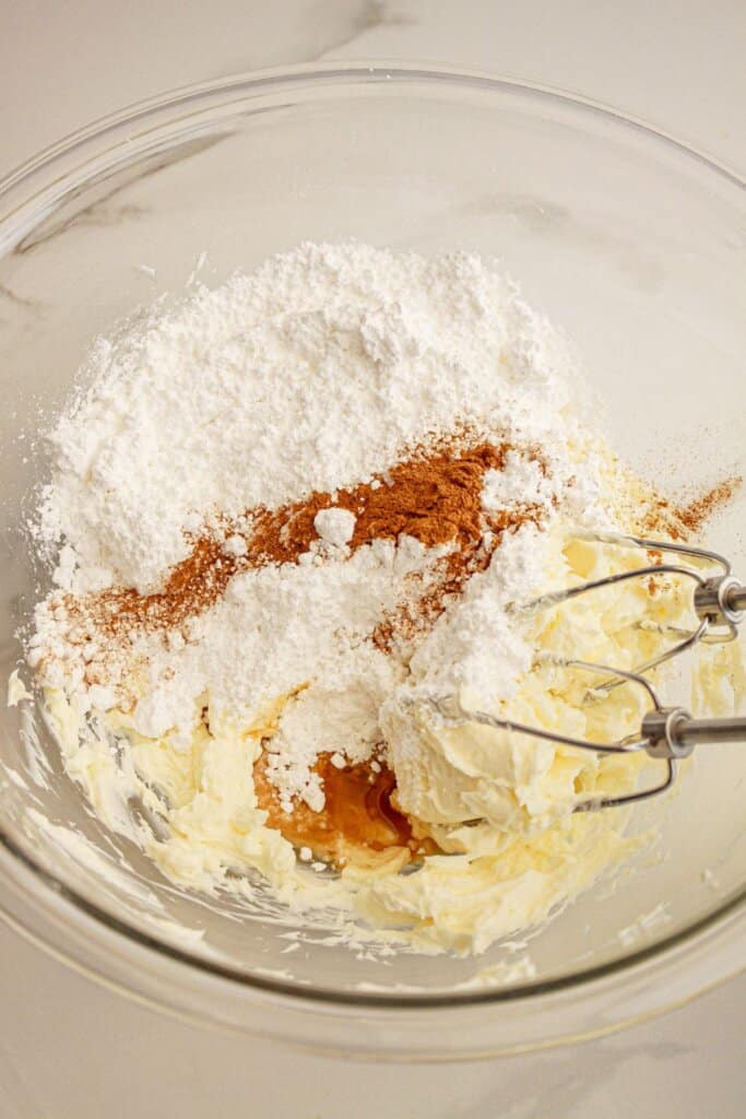 Cream cheese frosting being mixed in a glass mixing bowl.