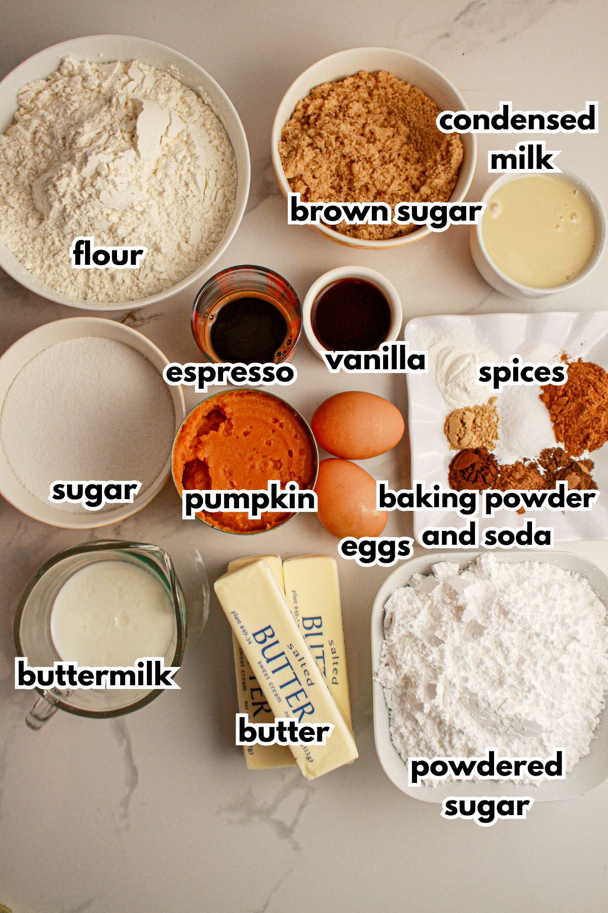 Flour, brown sugar, condensed milk, espresso, vanilla, sugar, pumpkin, eggs, baking powder and soda, spices, buttermilk, butter, and powdered sugar on a counter.