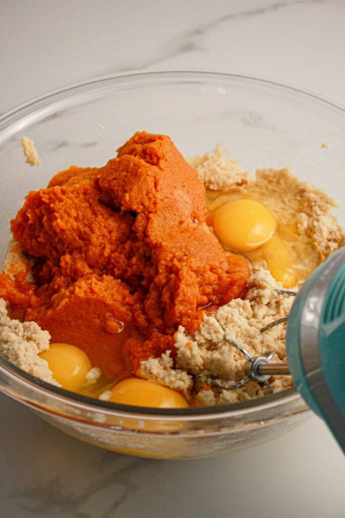 Pumpkin puree and eggs being mixed into batter in a glass mixing bowl.