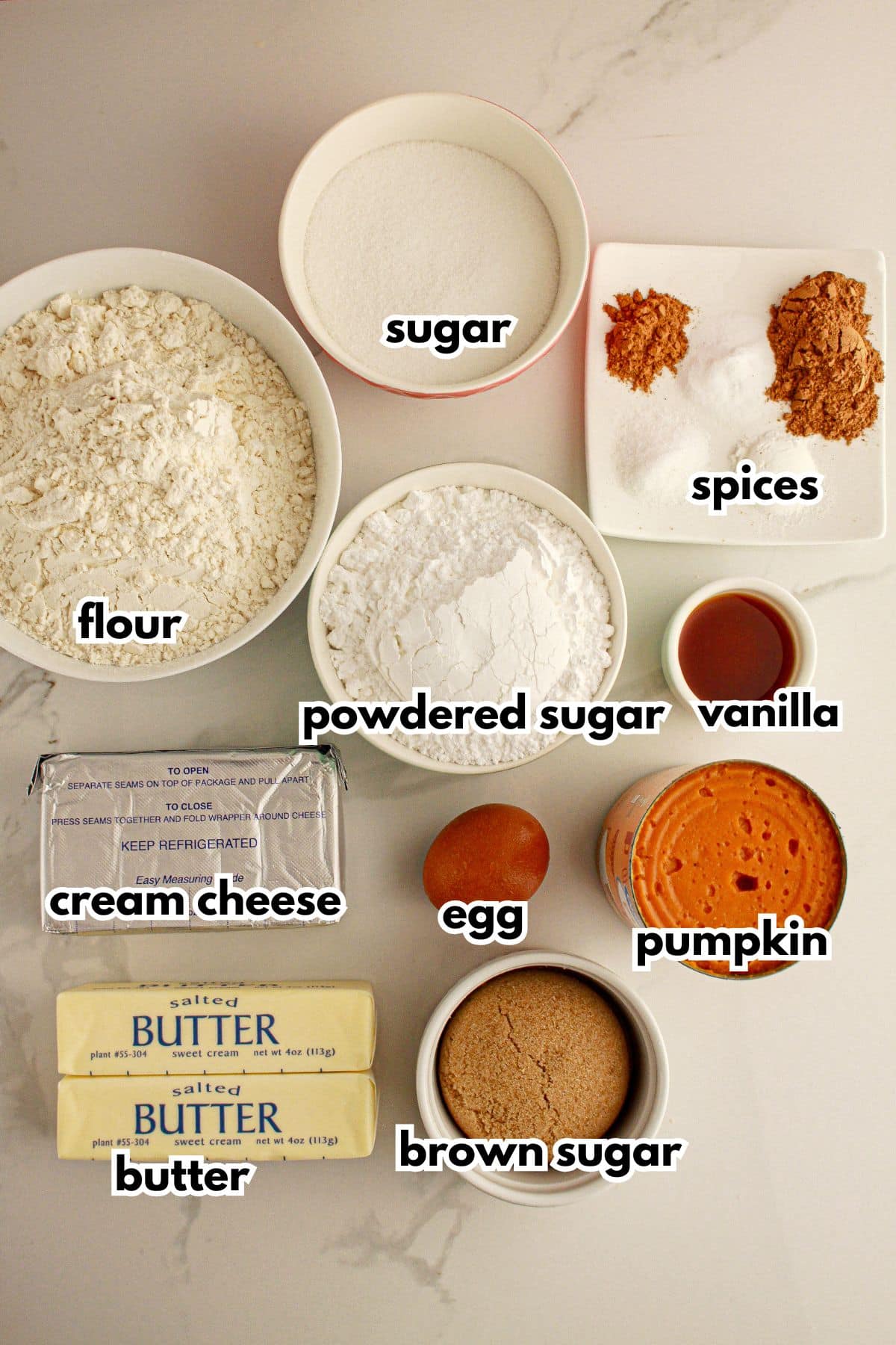 Bowls of sugar, flour, spices, powdered sugar, cream cheese, butter, egg, brown sugar, pumpkin, and vanilla.