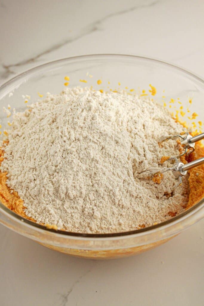 Dry ingredients being added to wet ingredients in a glass mixing bowl.