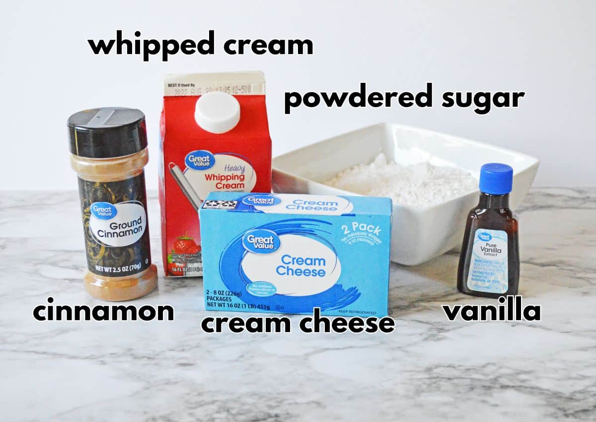 Whipped cream, powdered sugar, cream cheese, vanilla, and cinnamon on a counter.