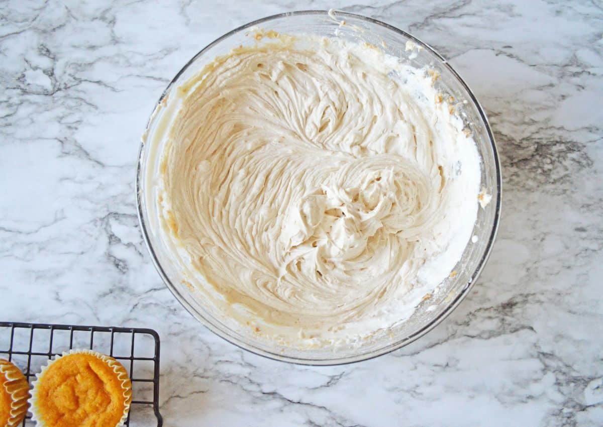 Frosting being mixed in a large glass mixing bowl.