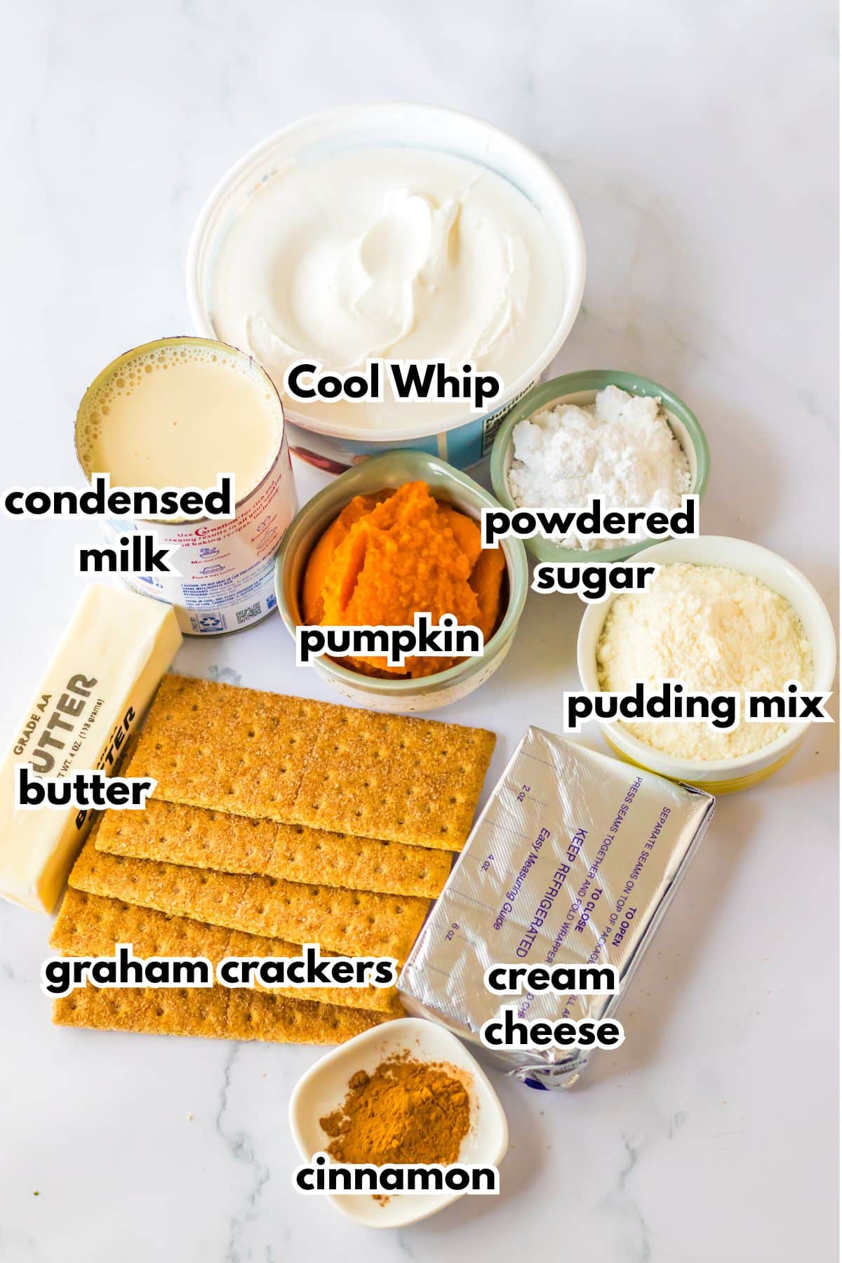 Bowls of Coll Whip, condensed milk, butter, graham crackers, pumpkin, powdered sugar, pudding mix, cream cheese, and cinnamon on a counter.