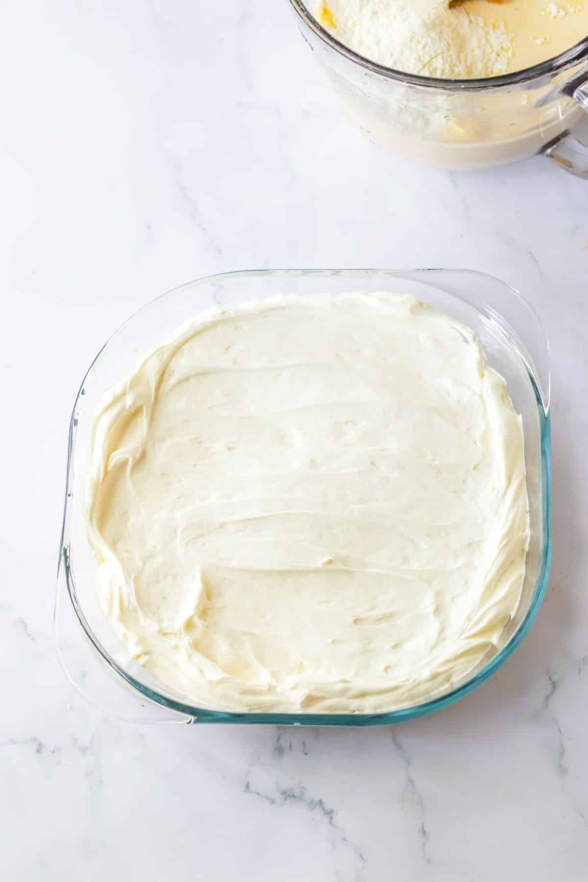 Cream cheese layer being spread on top of the dessert in the baking dish.