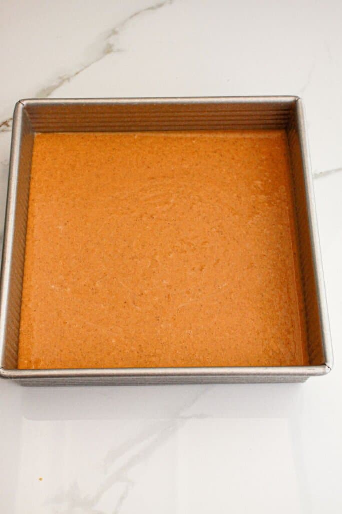 Pumpkin pie filling poured into a metal square baking dish.