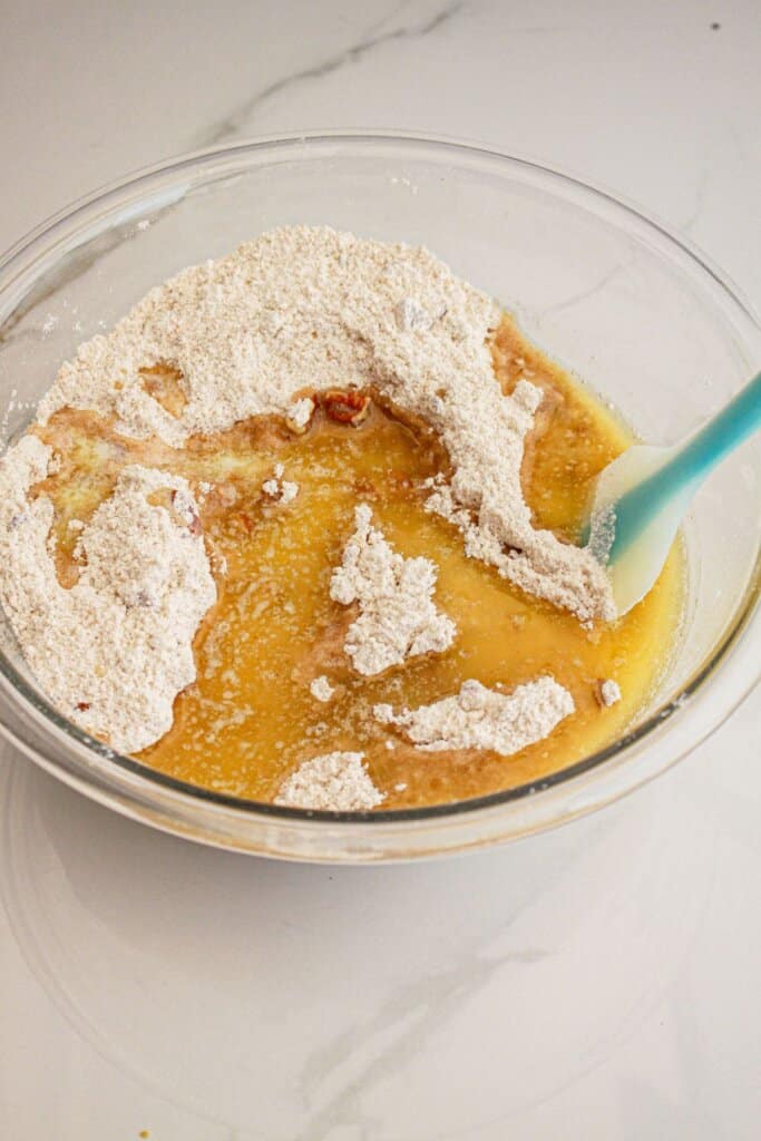 Melted butter being added to flour, brown sugar mixture in a large glass bowl.