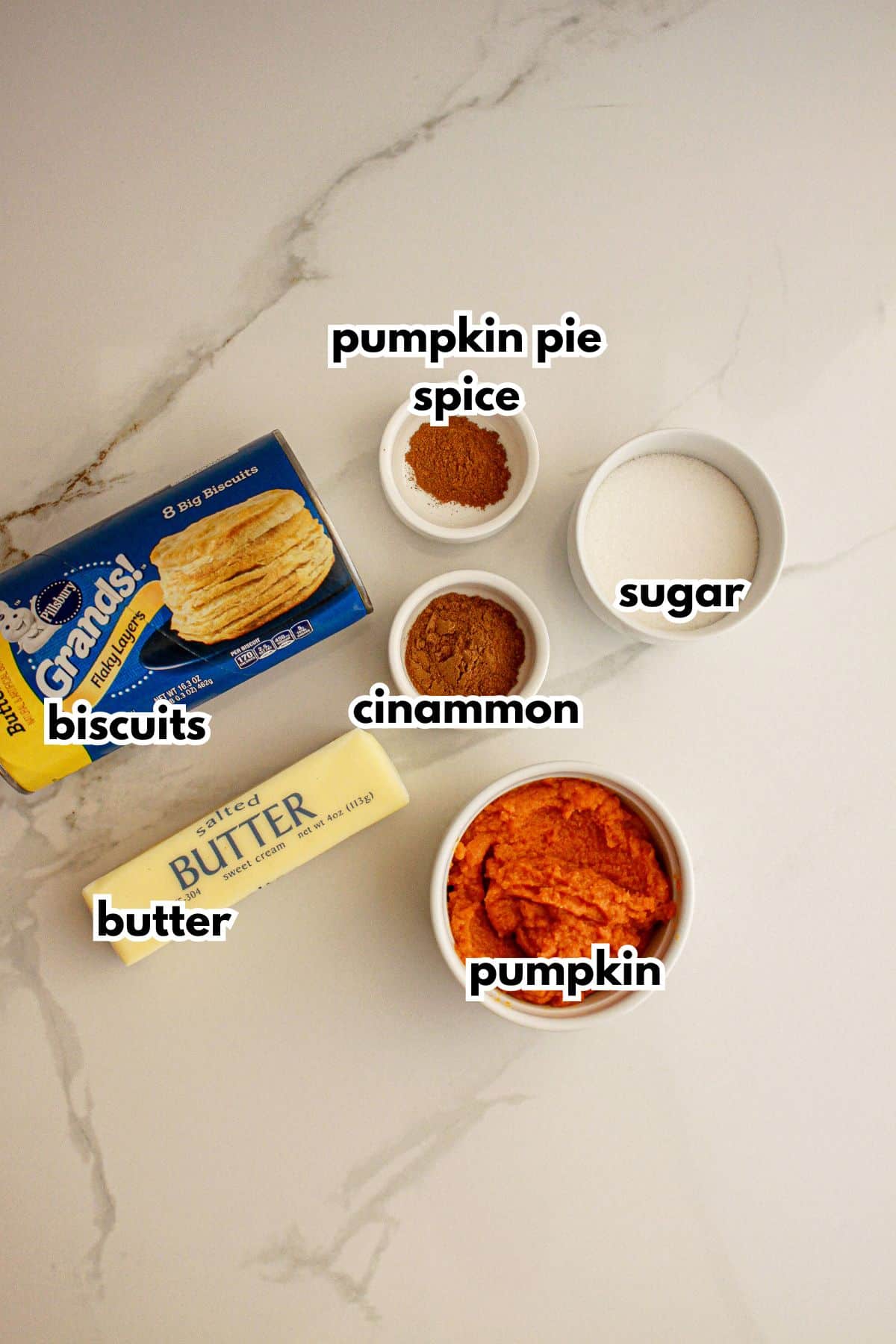 Bowls of biscuits, butter, pumpkin pie spice, cinnamon, sugar, and pumpkin on a counter.