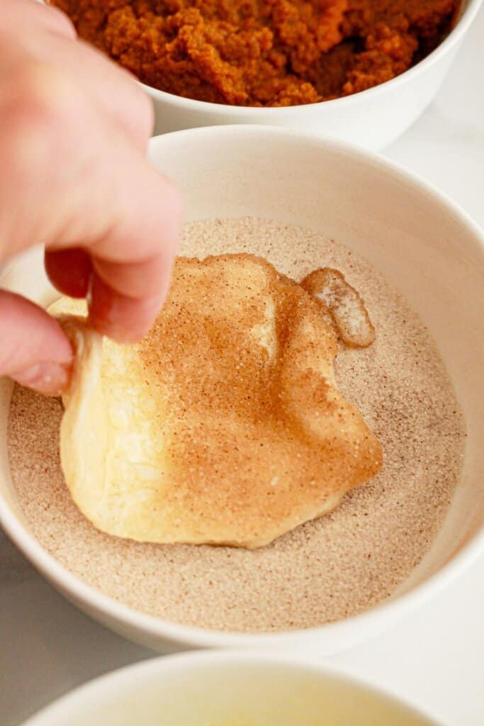 Biscuit piece being dipped in cinnamon sugar mixture.