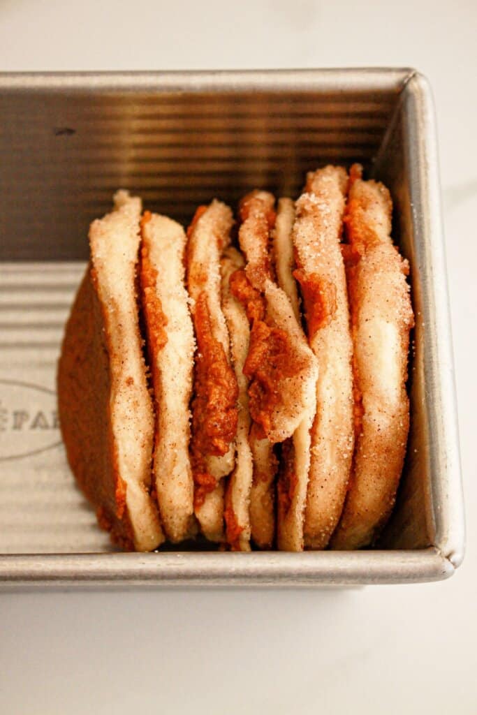 Pieces of biscuits being layered into a loaf pan.