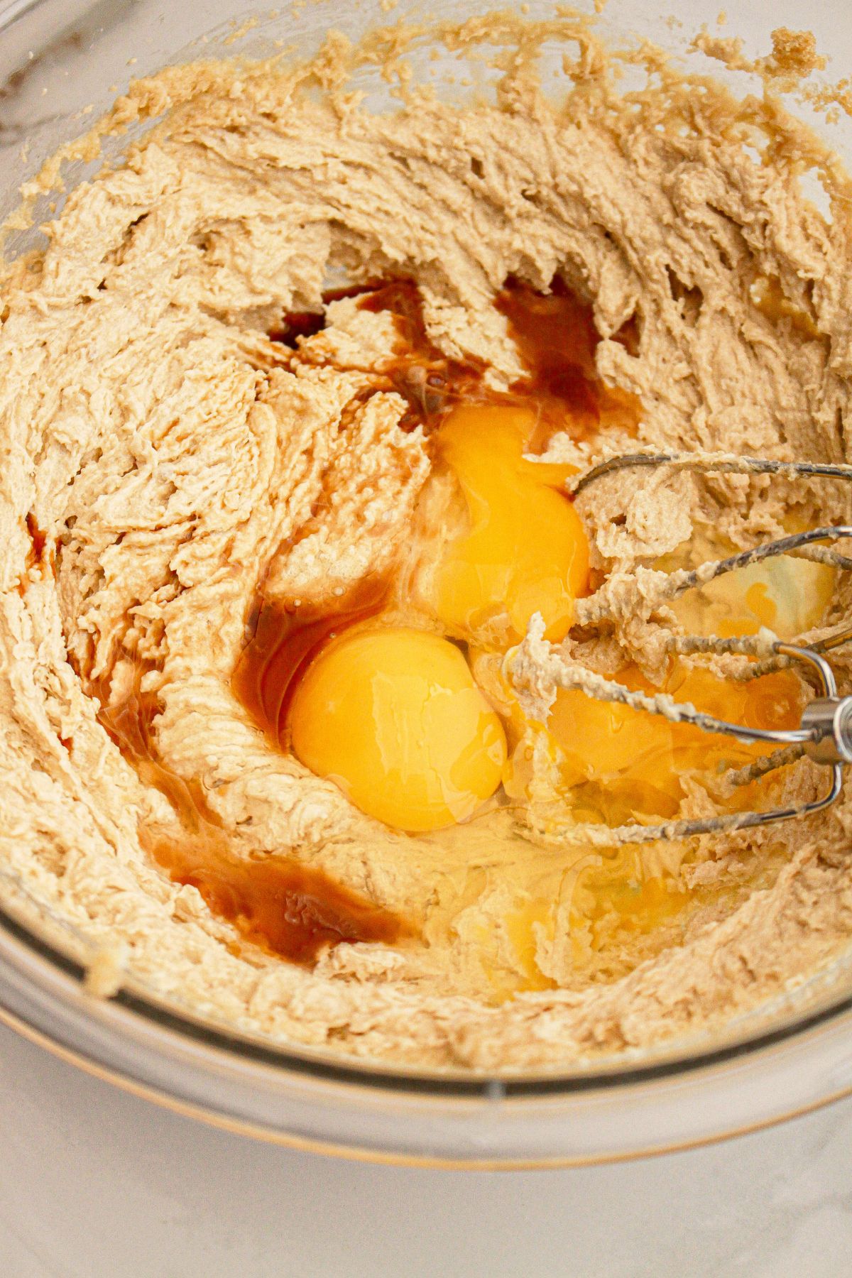 Eggs being added to cookie dough in a glass mixing bowl.