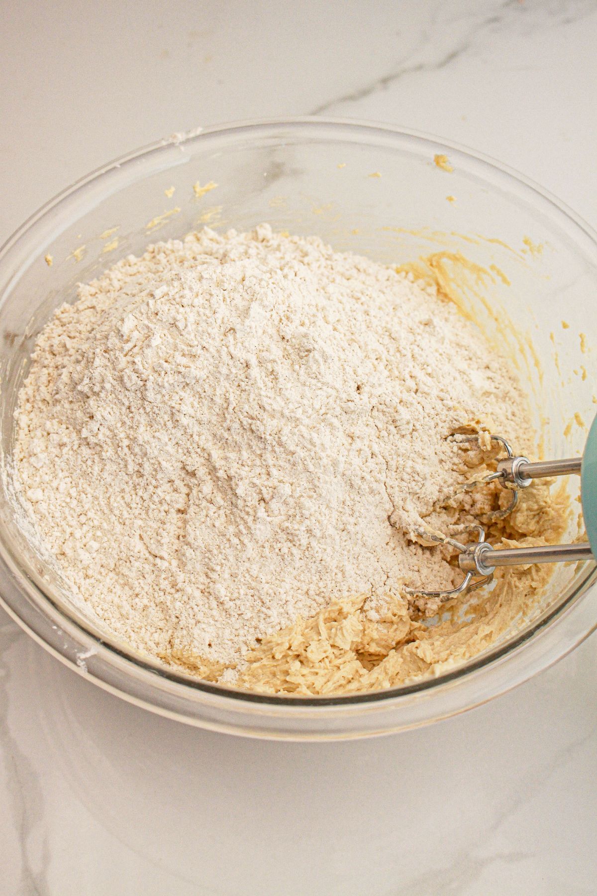 Dry ingredients being added to dough in a glass mixing bowl.