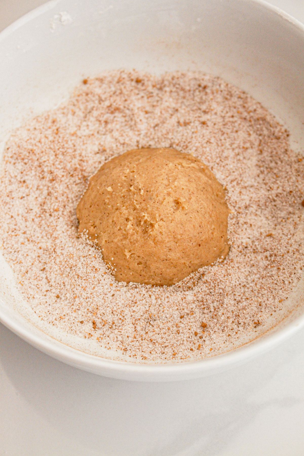 Cookie dough ball being rolled in cinnamon sugar.