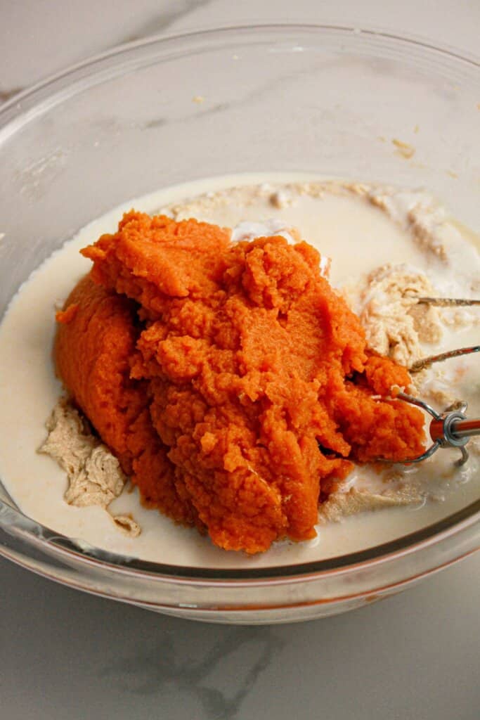 Pumpkin being mixed into batter in a glass mixing bowl.