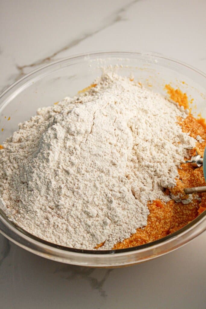 Dry ingredients being added to wet ingredients in a glass mixing bowl.