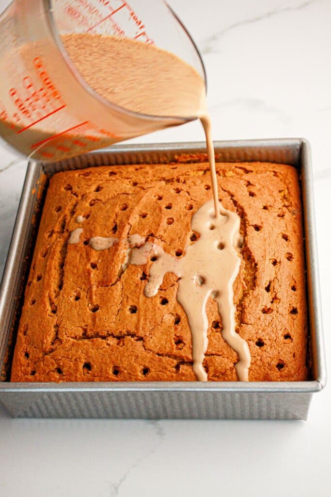 Pumpkin spice filling being poured over a cake in a baking pan.