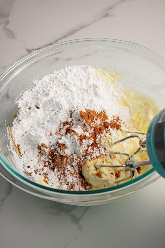 Frosting being mixed in a glass mixing bowl with a hand mixer.