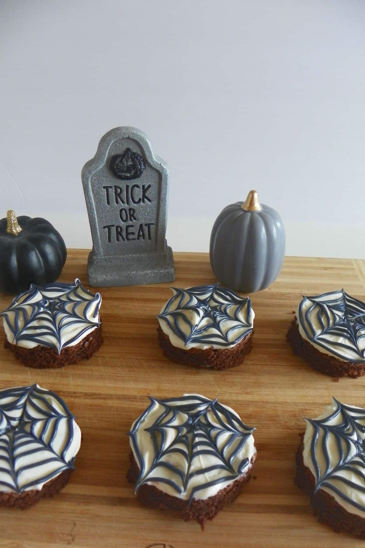 Six spider web brownie on a wooden cutting board.